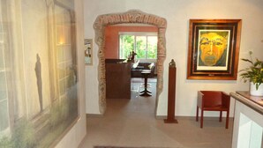 A hallway with a patterned rug, a framed painting, and a view into a dining area. - Garni Gardenia (Caslano)