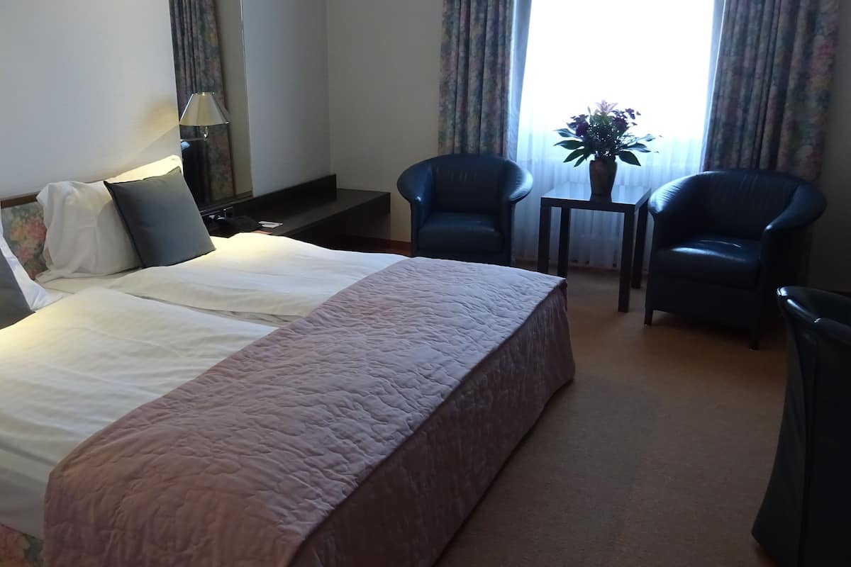 Habitación de hotel con una cama grande, dos sillas, una mesita y una ventana con cortinas.