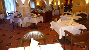 A restaurant with multiple tables set for dining, a central buffet area, and a patterned carpet.
