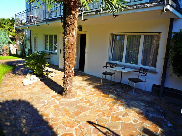 Una casa con un patio de piedra, una palmera y un balcón con sillas.