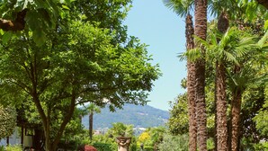 A patio with a table and chairs, surrounded by lush greenery and palm trees. - Garni Gardenia (Caslano)