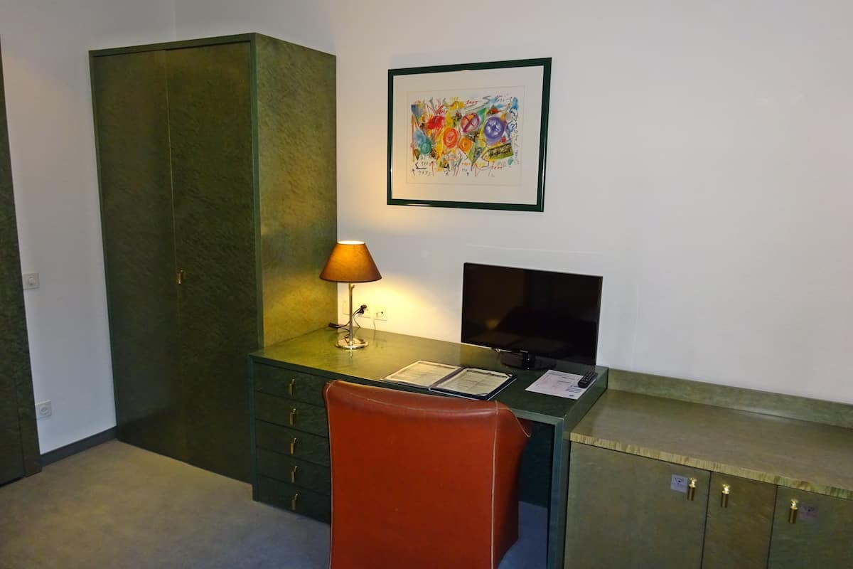 Un pequeño espacio de oficina con un escritorio, una silla, una lámpara, un televisor y una obra de arte enmarcada en la pared.