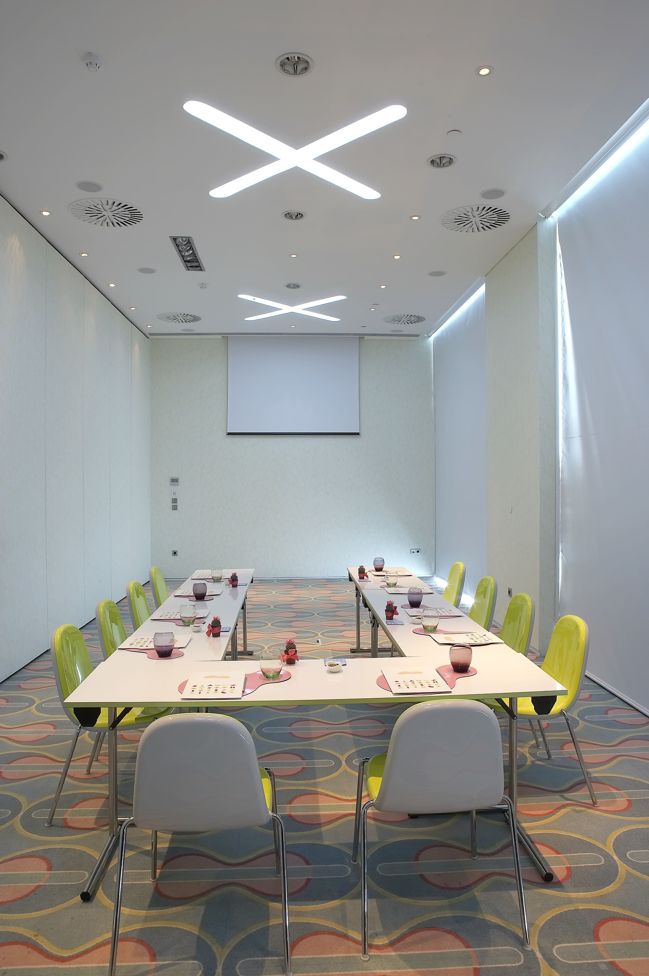 A conference room with a long table, chairs, a projector screen, and ceiling lights.