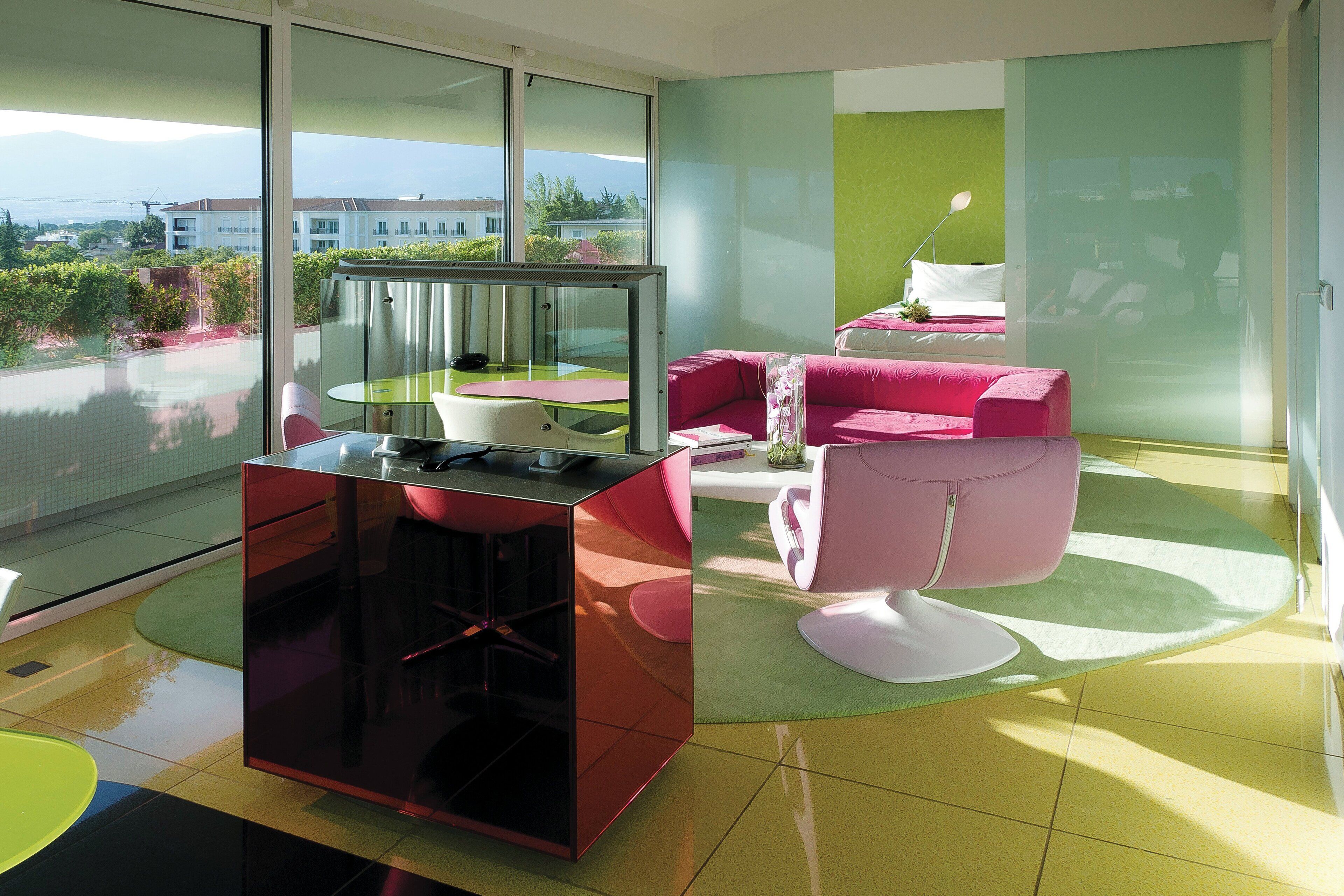 Una sala de estar moderna con un separador de vidrio, un sofá rosa, un sillón blanco y una mesa de centro de vidrio.