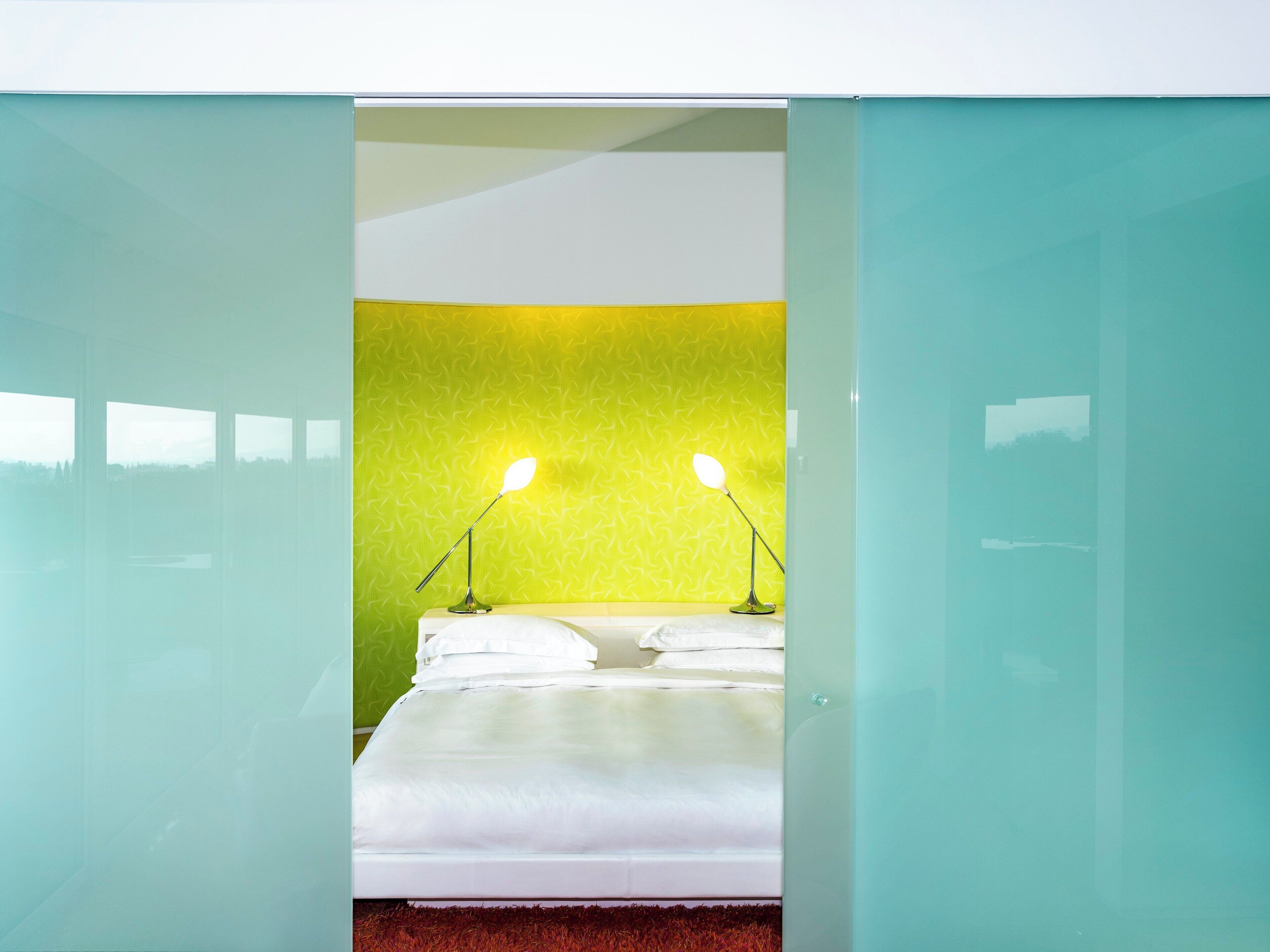 Habitación de hotel moderna con una cama, dos lámparas de noche y una pared de acento verde.