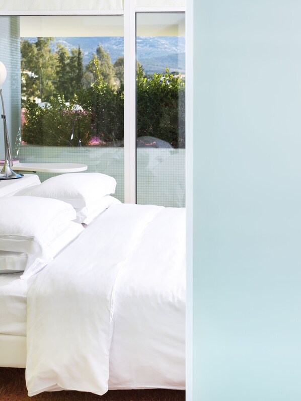 Habitación de hotel con cama, mesita de noche y un gran ventanal con vistas a árboles y montañas.