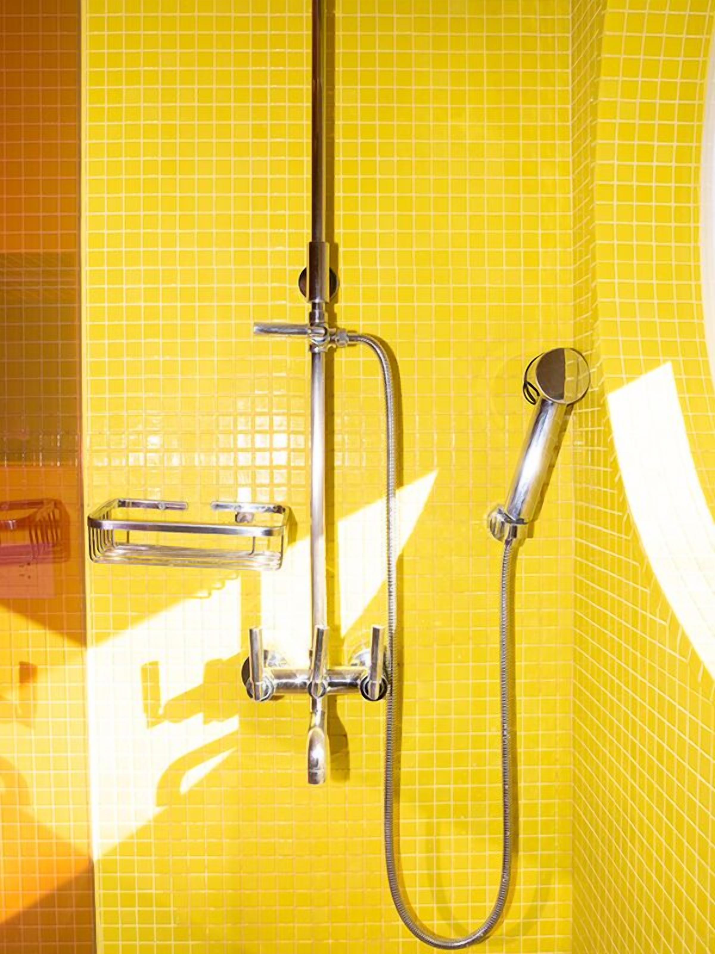 Una ducha con grifería cromada y pared revestida de azulejos amarillos.