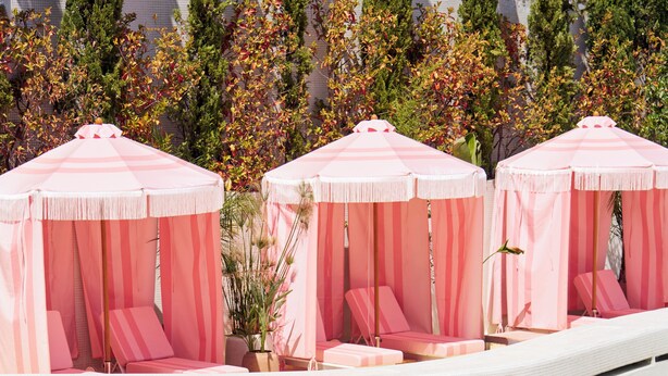 Zona de piscina con asientos escalonados y toldos rosas.