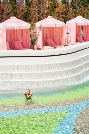 Zona de piscina con asientos escalonados y toldos rosas.