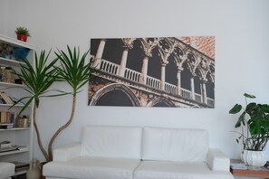 A white sofa, a bookshelf, and a large framed picture of a building's facade. - Hotel Paris (Mestre)