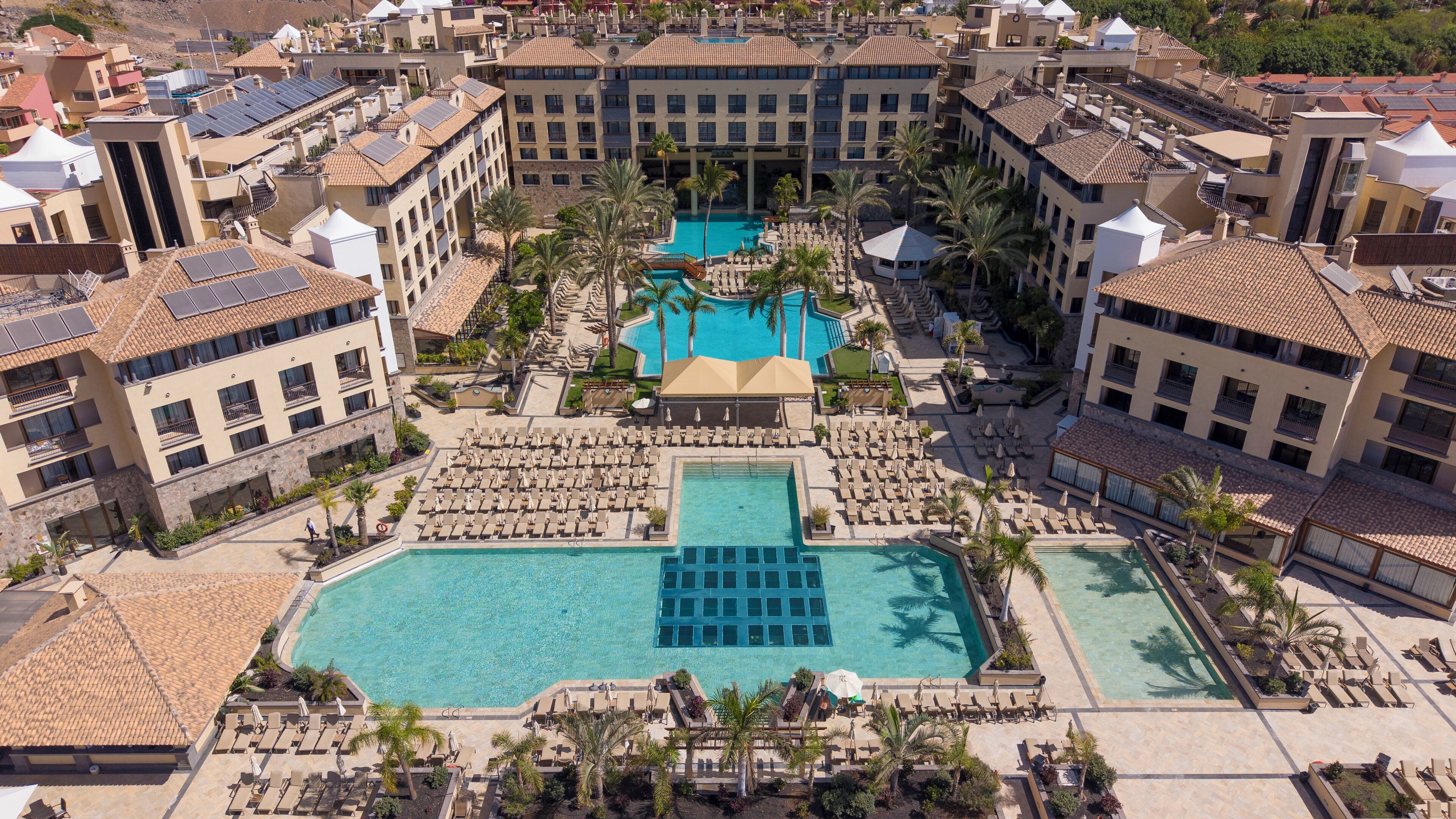A resort with multiple swimming pools, sun loungers, and palm trees.