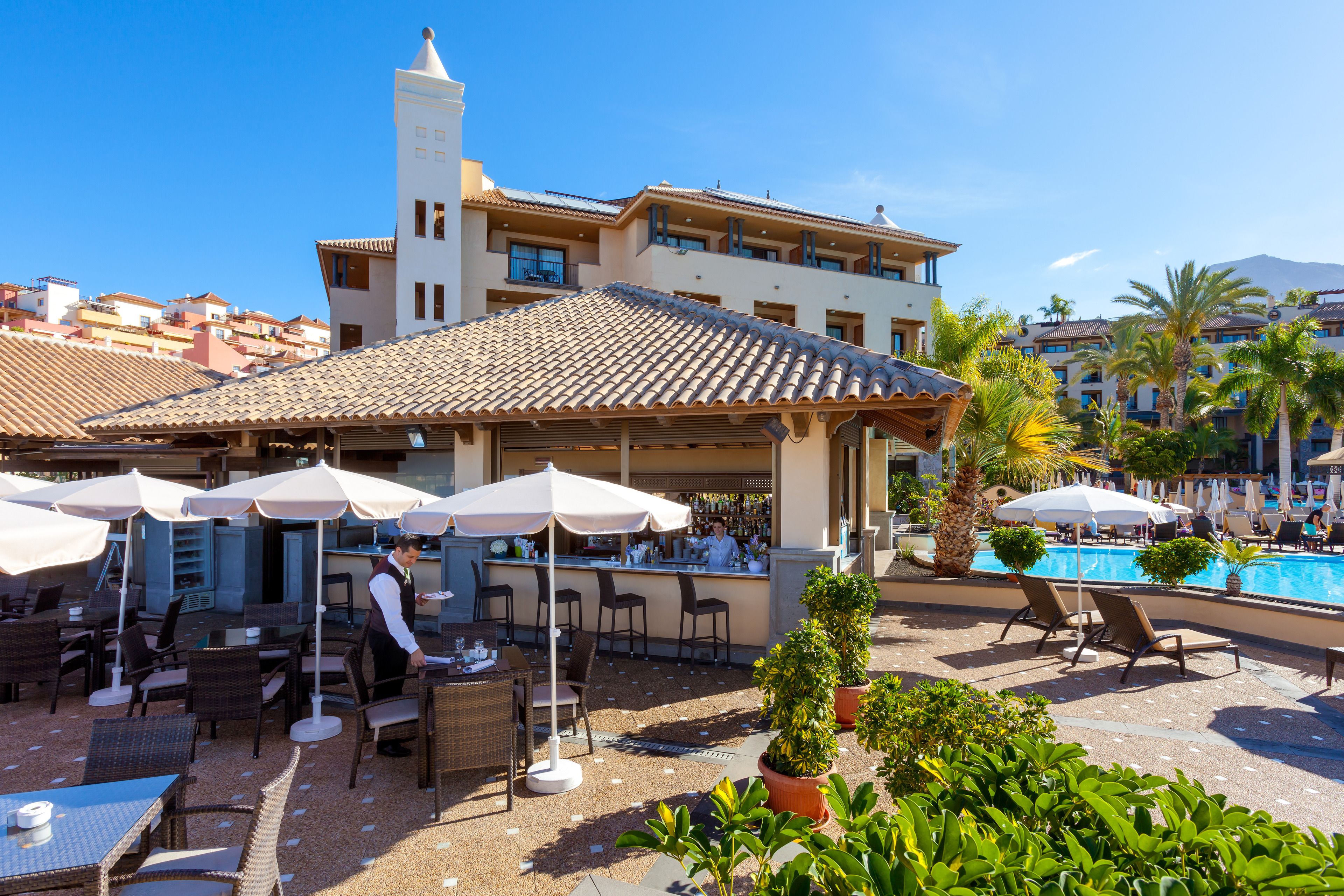 Un patio de hotel con mobiliario exterior, piscina y zona de bar.