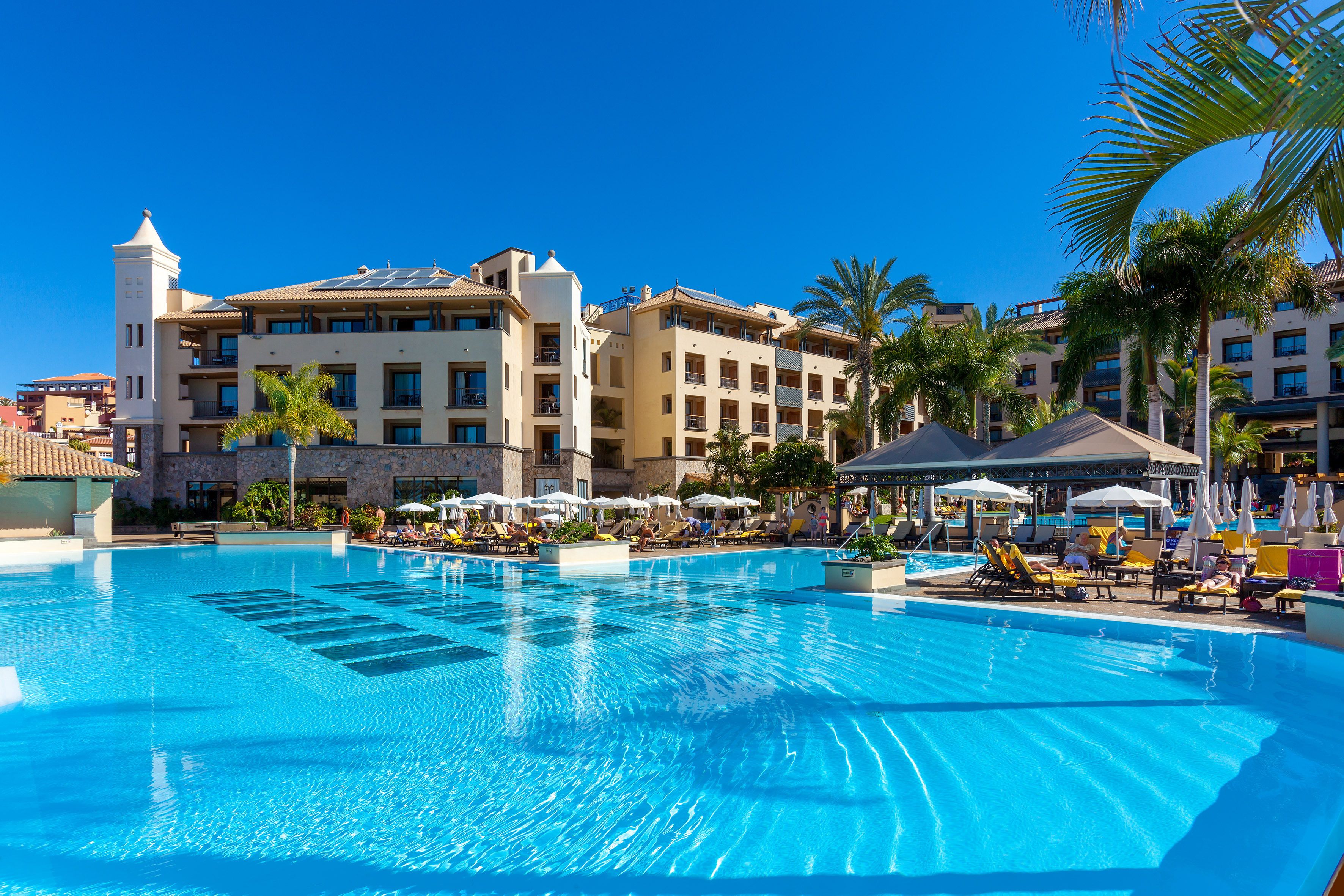 Un hôtel doté d’une grande piscine, de chaises longues et de palmiers.