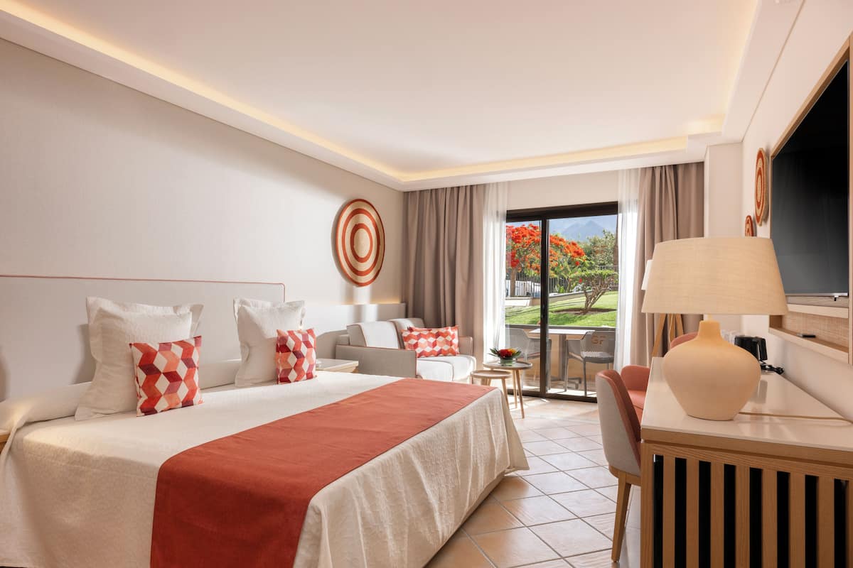 A hotel room with a large bed, a desk, a chair, a TV, and a view of the outdoors.