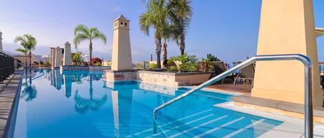 A swimming pool with clear blue water, surrounded by palm trees and a tower structure.