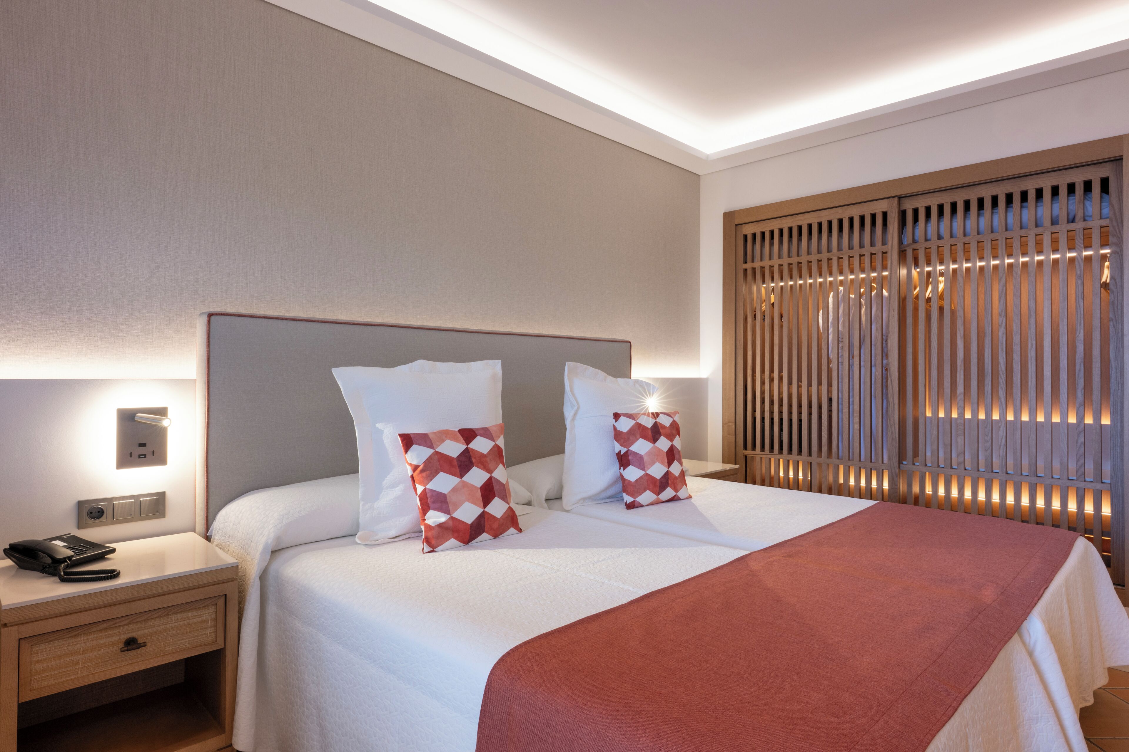 A hotel room with a large bed, two pillows, a bedside table with a phone, and a nightstand.