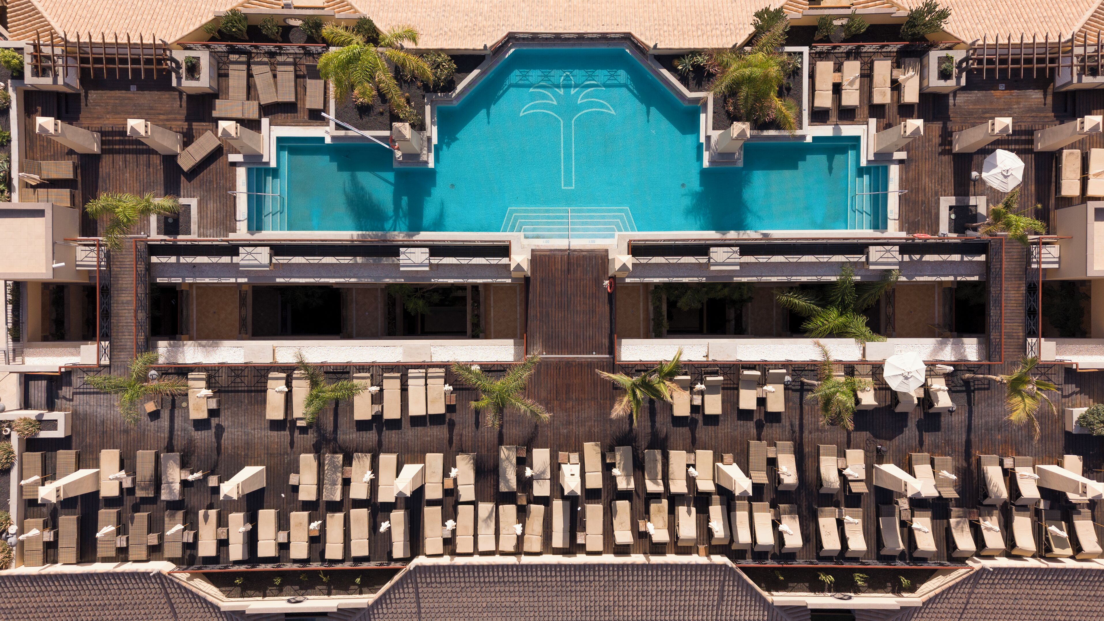 Un resort con una piscina central, varias zonas de descanso y un diseño arquitectónico simétrico.