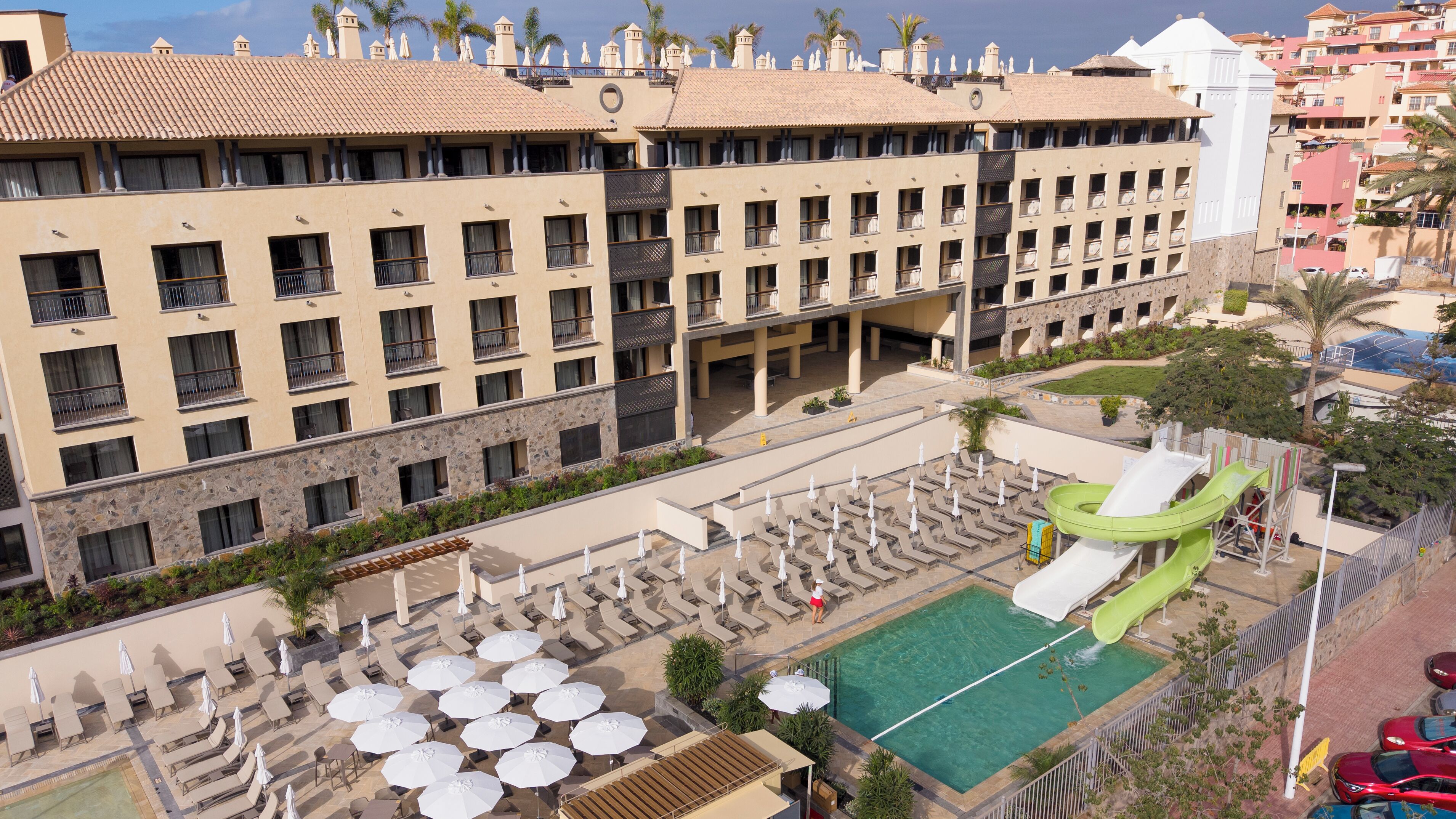 A hotel with multiple floors, outdoor swimming pool, and a children's play area with slides.