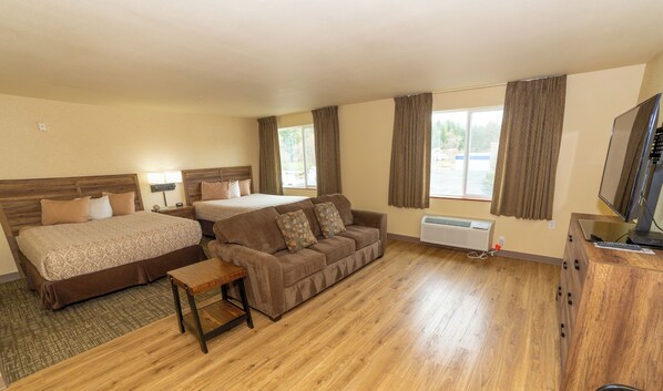 A hotel room with two beds, a sofa, a small table, a TV, and a window with curtains.