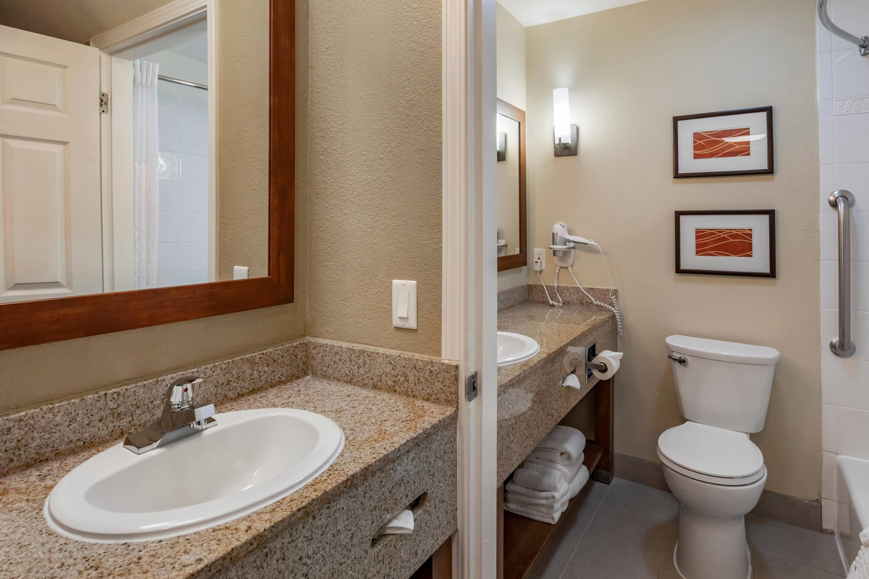 A bathroom with a granite countertop sink, a white toilet, and a shower area.