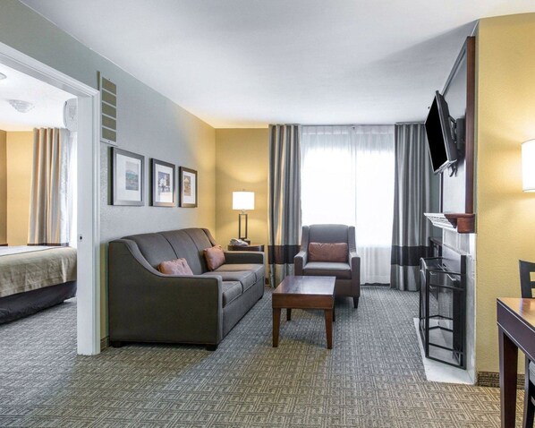 Une chambre d’hôtel équipée d’un canapé, d’un fauteuil, d’une table basse et d’un téléviseur posé sur un meuble.