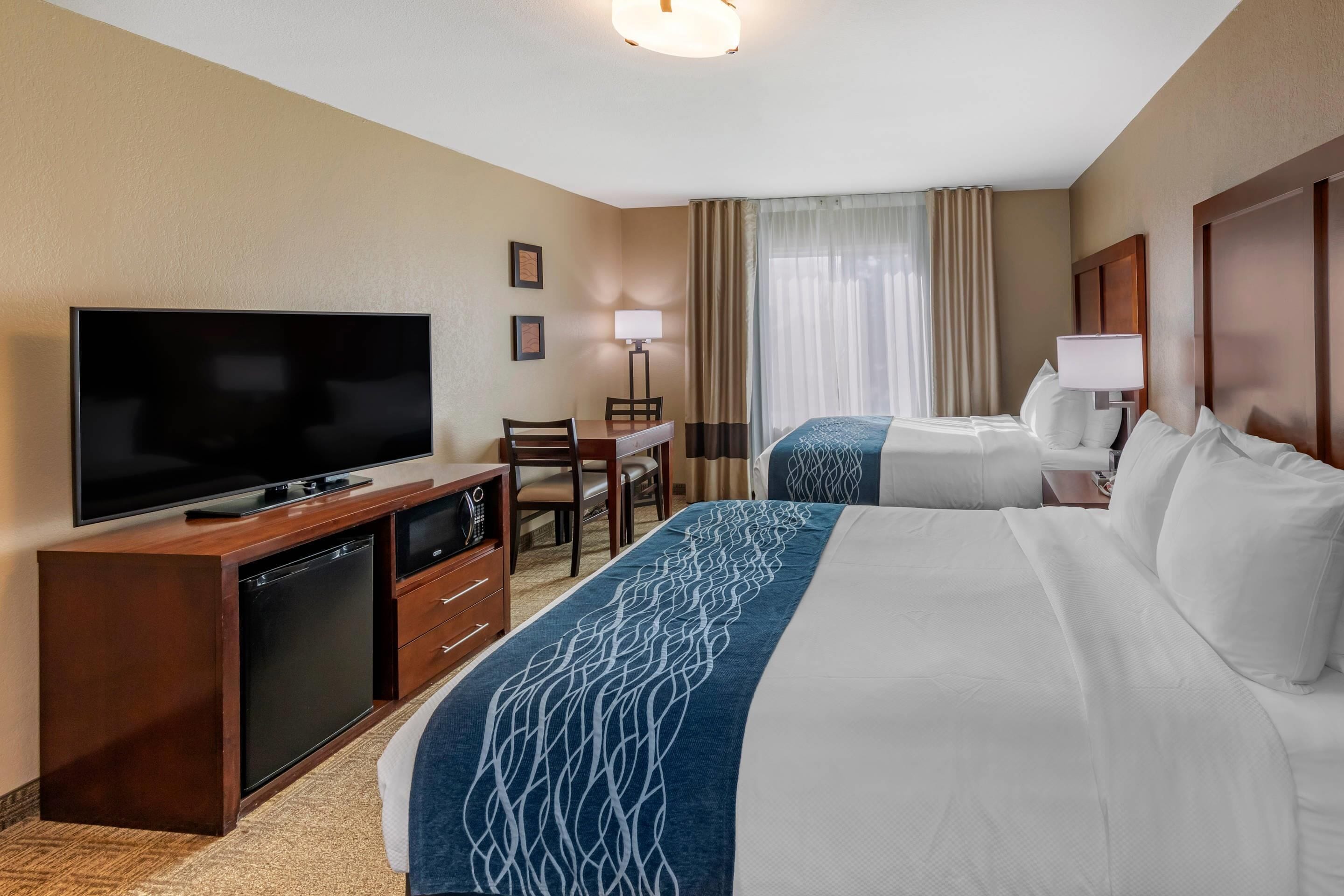 Ein Hotelzimmer mit zwei Betten, einem Fernseher, einem Schreibtisch mit Stuhl und einer Lampe.