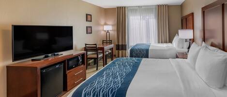 Ein Hotelzimmer mit zwei Betten, einem Fernseher, einem Schreibtisch mit Stuhl und einer Lampe.