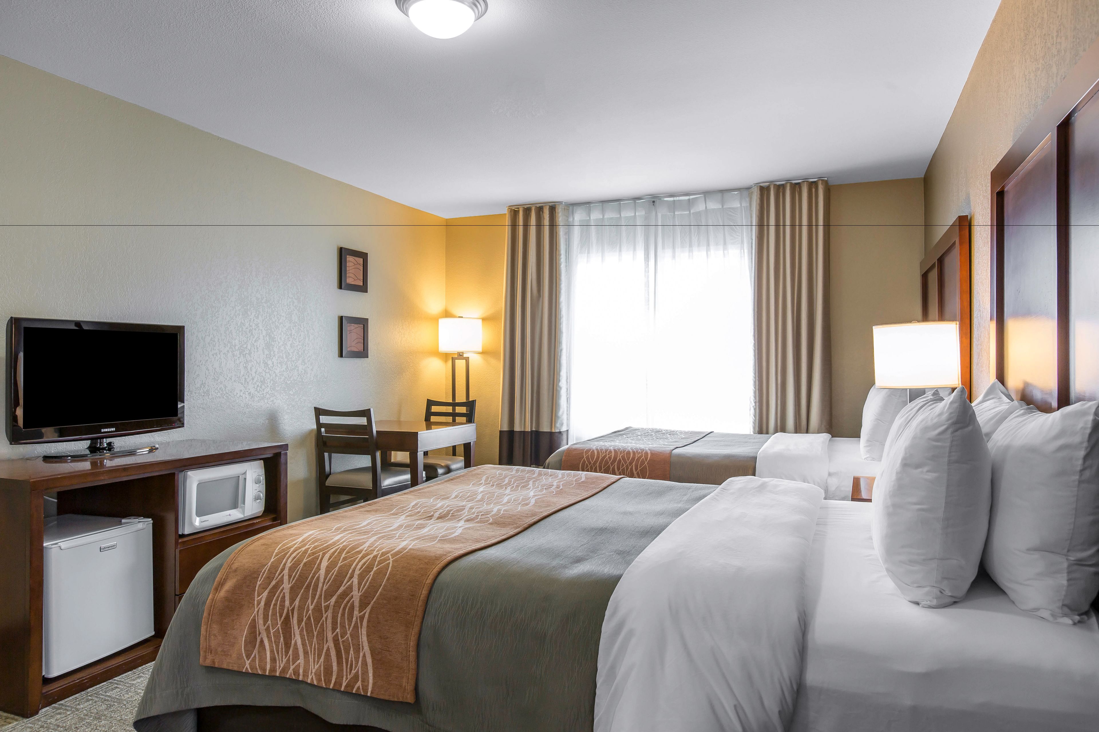 A hotel room with two beds, a TV, a mini-fridge, a desk, and a chair.