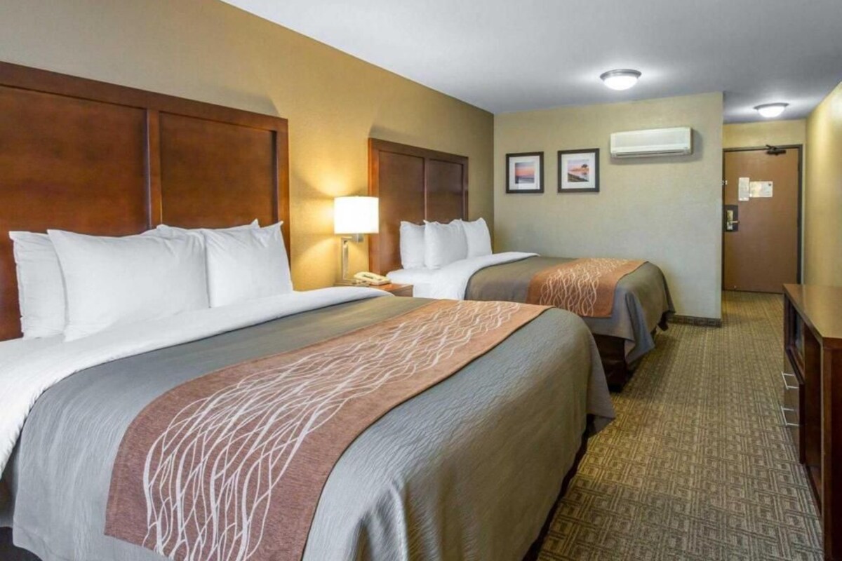 Una habitación de hotel con dos camas, un escritorio, una lámpara y una puerta.