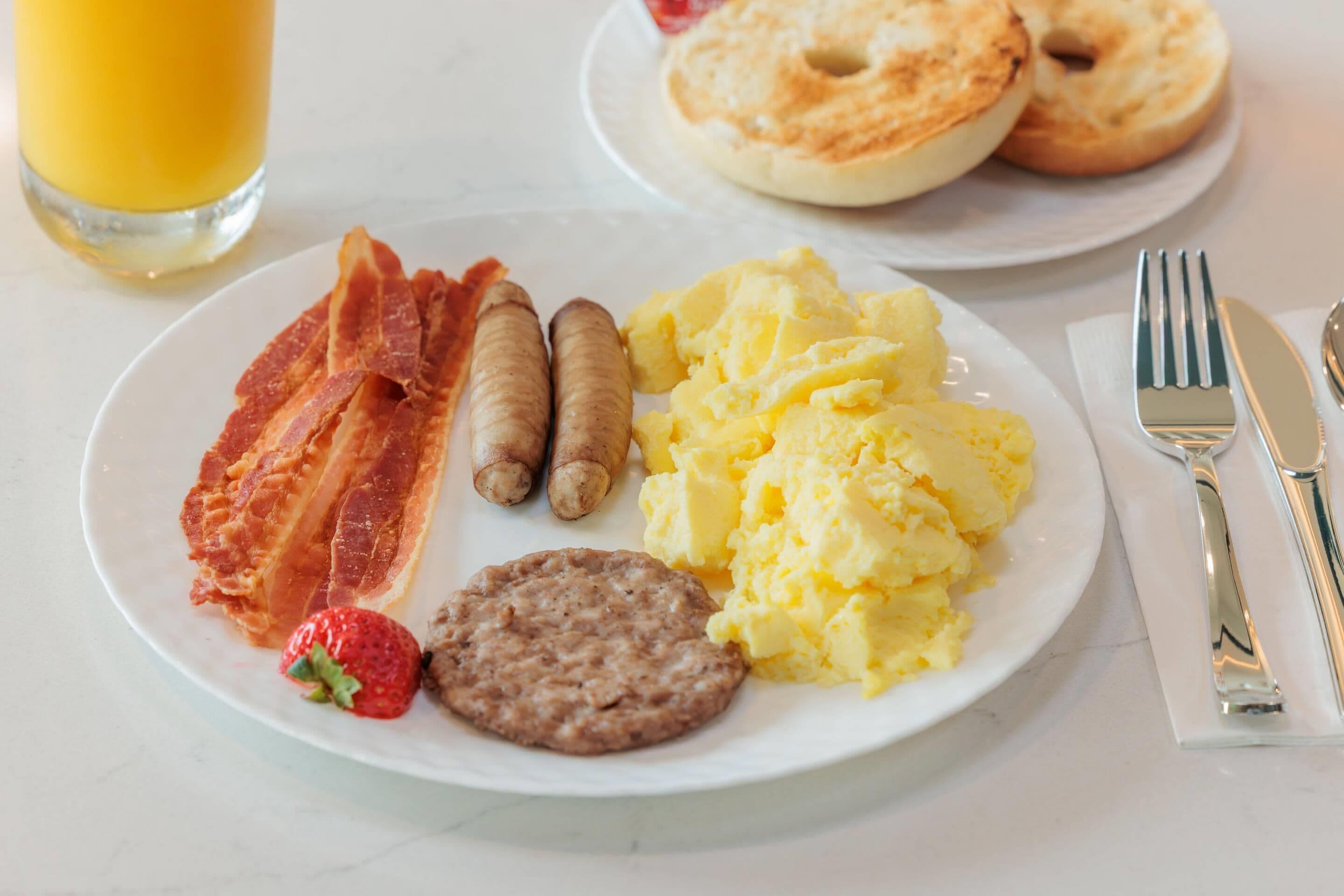 A breakfast plate with bacon, sausages, scrambled eggs, a strawberry, and a biscuit.