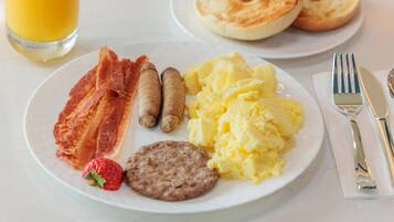 A breakfast plate with bacon, sausages, scrambled eggs, a strawberry, and a biscuit.