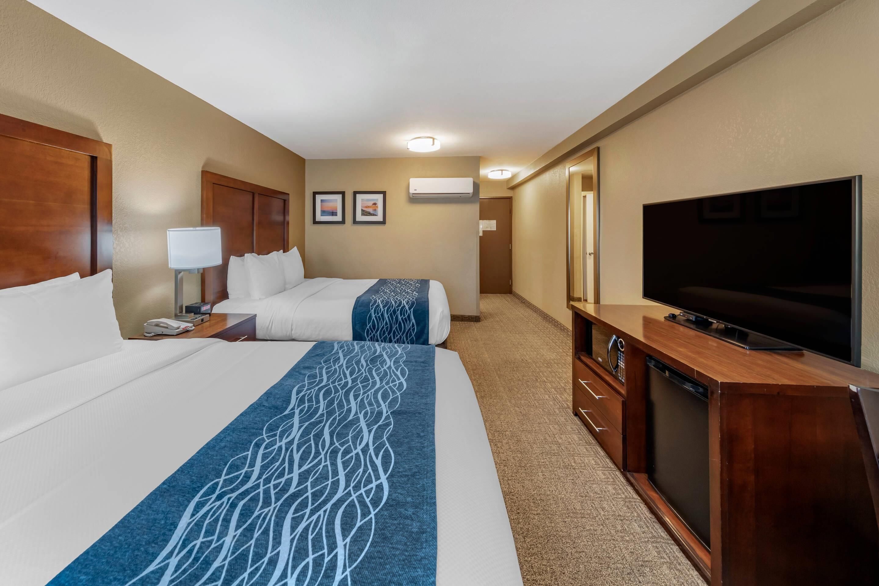 A hotel room with two beds, a TV, a desk with a lamp, and a dresser.