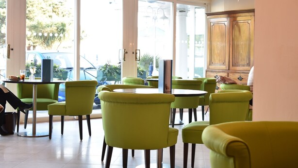 A room with green chairs and tables, large windows, and a chandelier. - Hermitage Hotel OCEANA COLLECTION (Bournemouth)
