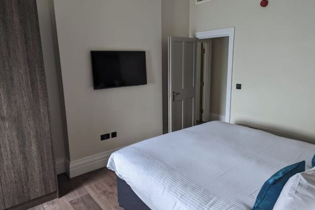 A bedroom with a bed, a television mounted on the wall, and a door leading to another room.