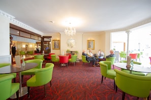 A hotel lobby with green chairs, a red carpet, and a chandelier.