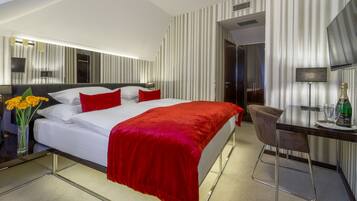 Quarto de hotel com cama, escrivaninha, cadeira, espelho e uma garrafa de champanhe.