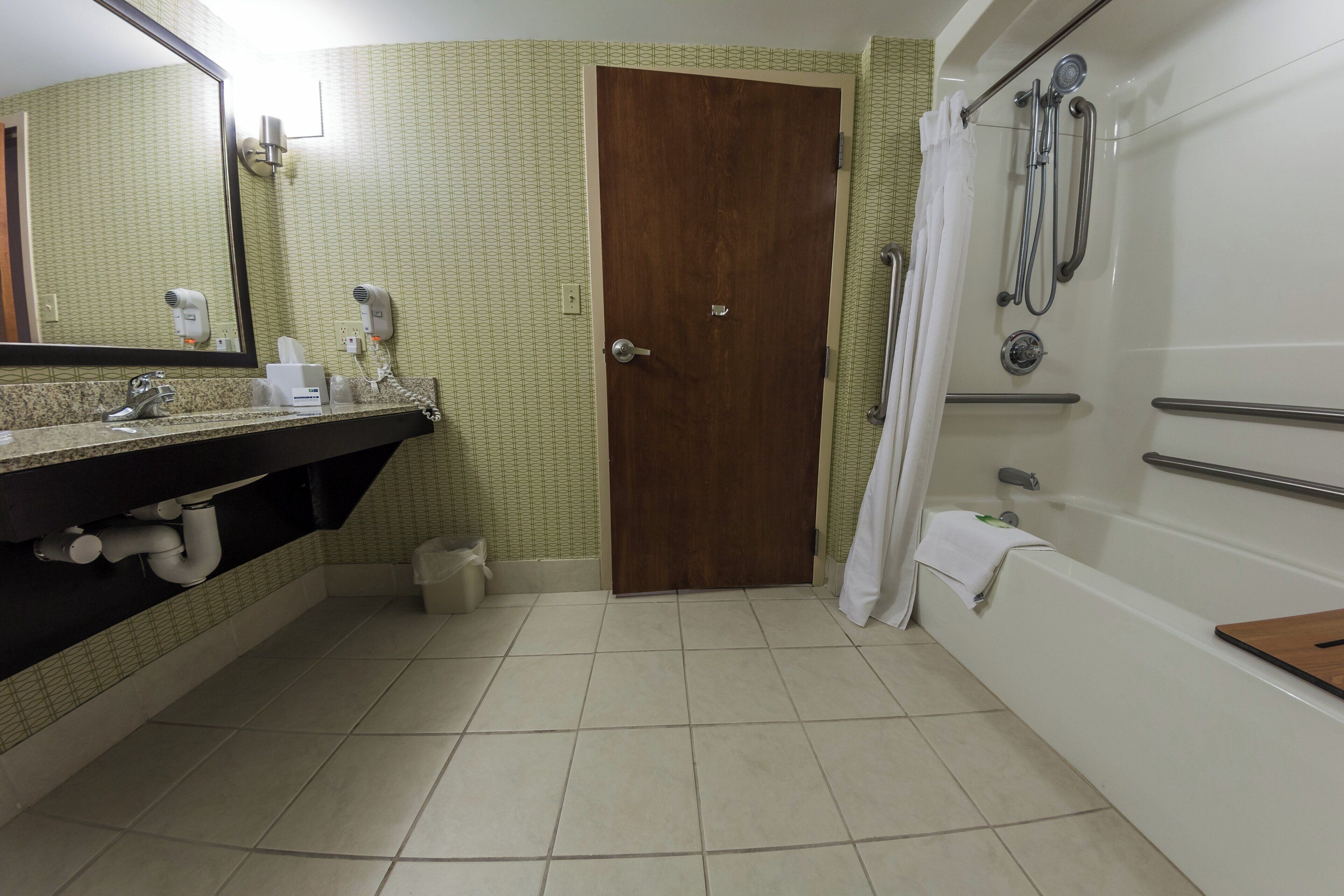 A bathroom with a wooden door, a sink with a mirror, a shower with a curtain, and a towel rack.