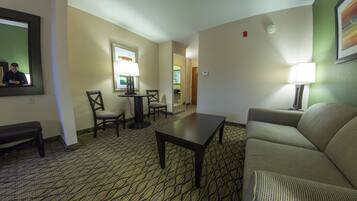A hotel room with a sofa, a small table, a chair, a lamp, and a mirror.