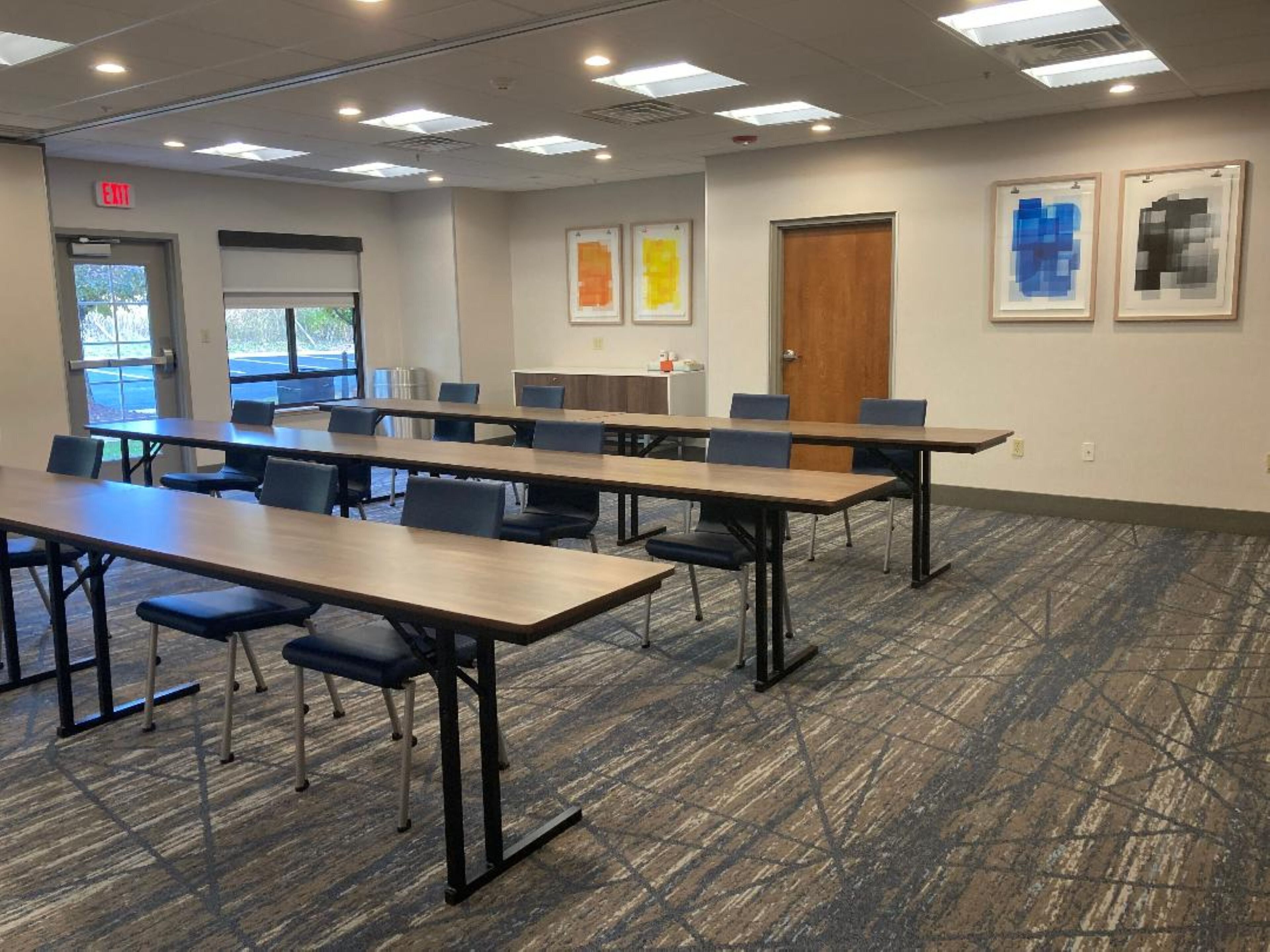 A conference room with long tables and chairs, a door, and framed artwork on the walls.