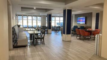 A modern dining area with tables and chairs, large windows, and a flat-screen TV mounted on the wall.