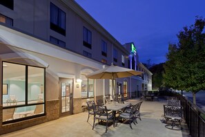 An outdoor patio area with tables and chairs, a pool, and a hotel building with a green sign. - Holiday Inn Express Hotel & Suites Winchester by IHG (Winchester)