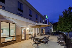 Un patio exterior con mesas y sillas, una piscina y un edificio de hotel con un letrero verde.
