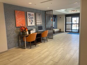A reception area with a desk, two chairs, a vase of flowers, and framed artwork on the wall. - Holiday Inn Express Hotel & Suites Winchester by IHG (Winchester)