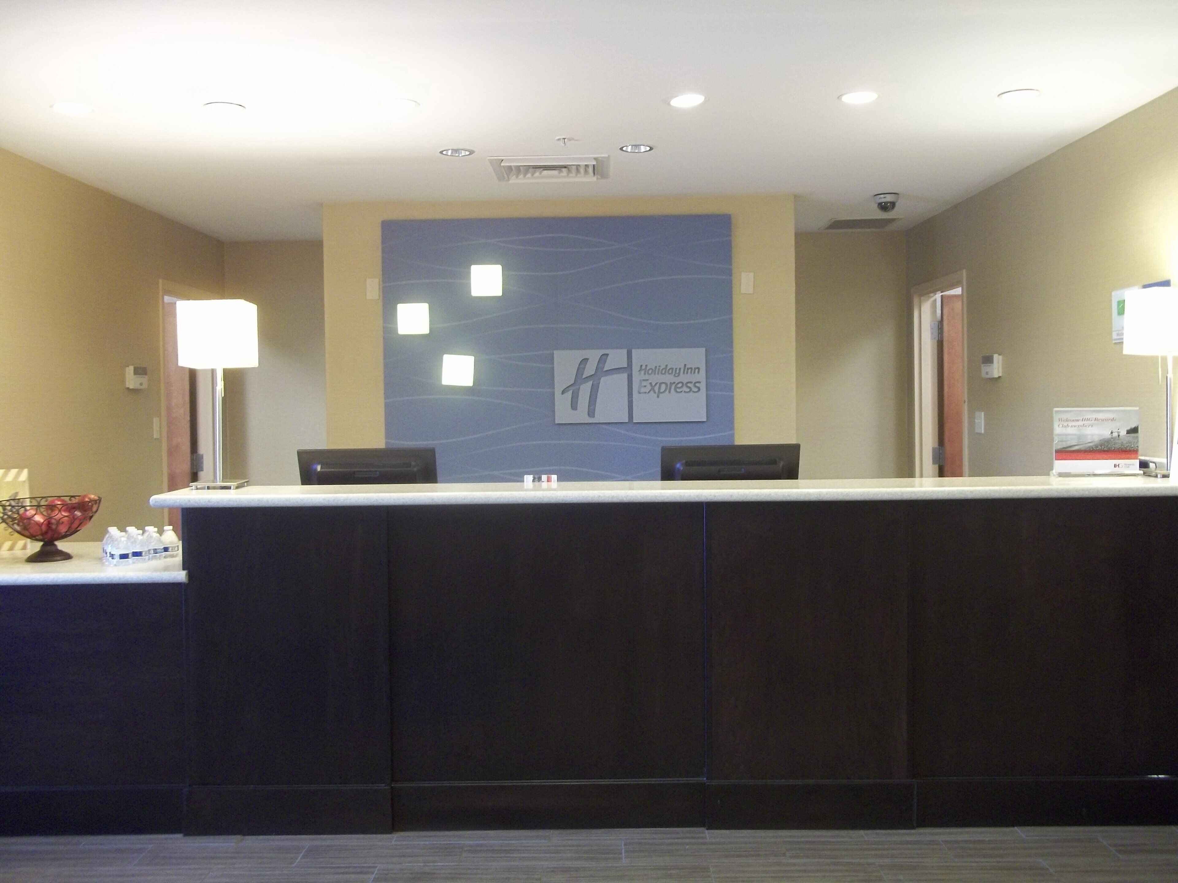 A reception desk with a Holiday Inn Express sign, a glass display case with water bottles, and a fruit bowl.