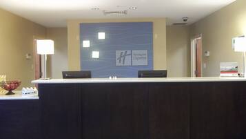 A reception desk with a Holiday Inn Express sign, a glass display case with water bottles, and a fruit bowl.