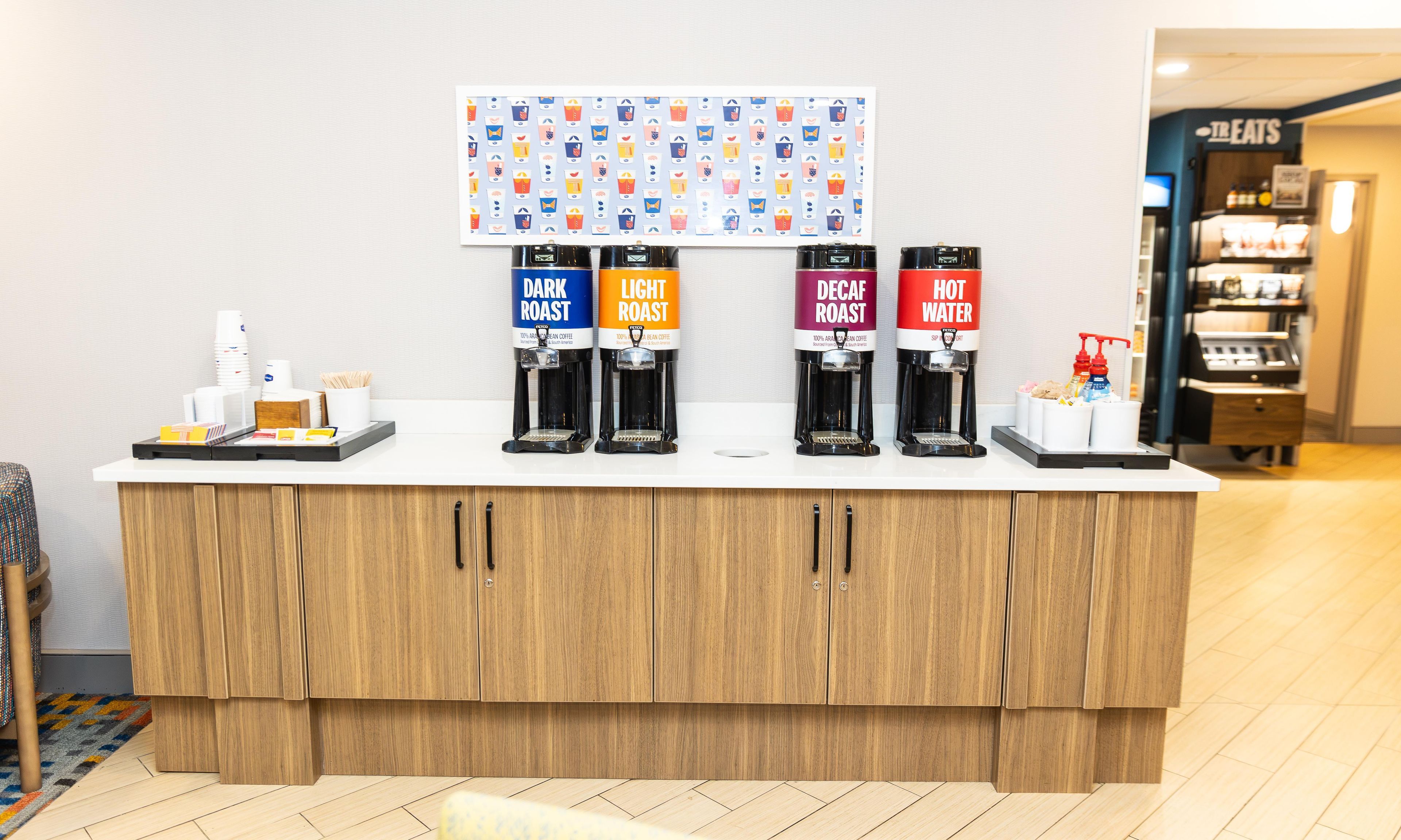 A coffee station with four dispensers labeled dark roast, light roast, decaf roast, and hot water.