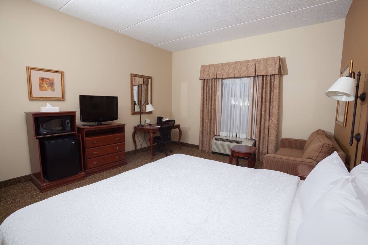 Habitación de hotel con una cama grande, un escritorio con silla, televisión, microondas y una ventana con cortinas.