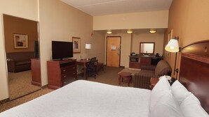 A hotel room with a large bed, a desk, a chair, a television, and a bathroom visible through an open door. - Hampton Inn Oneonta (Oneonta)