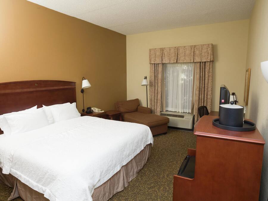 Una habitación de hotel con una cama grande, un escritorio con lámpara, una silla, un teléfono y una ventana con cortinas.