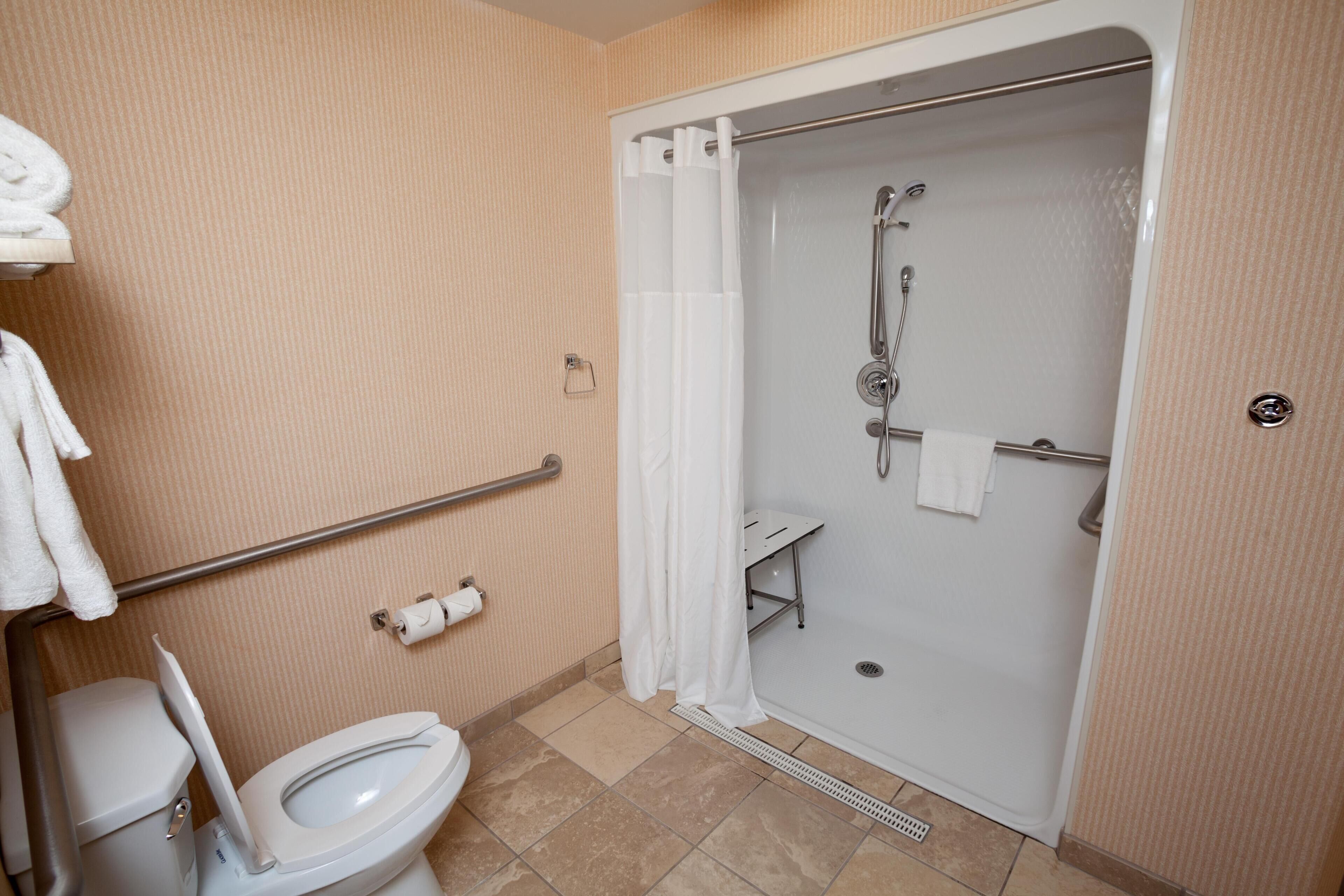 Une salle de bain équipée de toilettes, d’une douche avec une barre d’appui et d’un porte-serviettes.